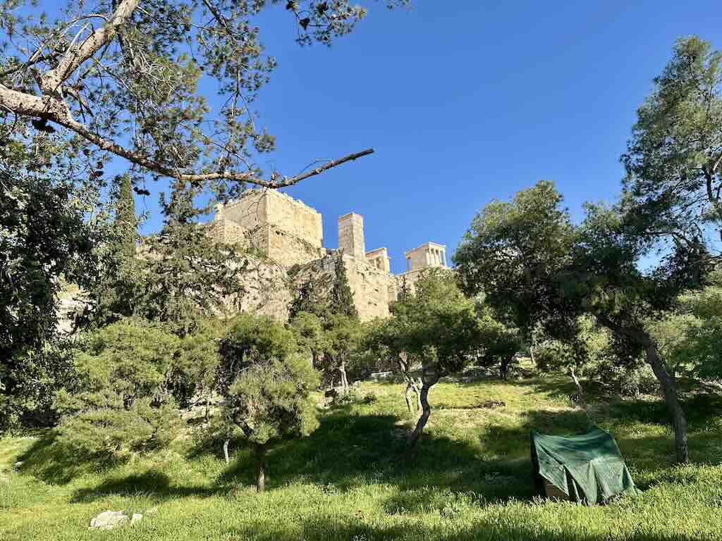 Acropolis of Athens seen from the slopes below with greenery and historic ruins