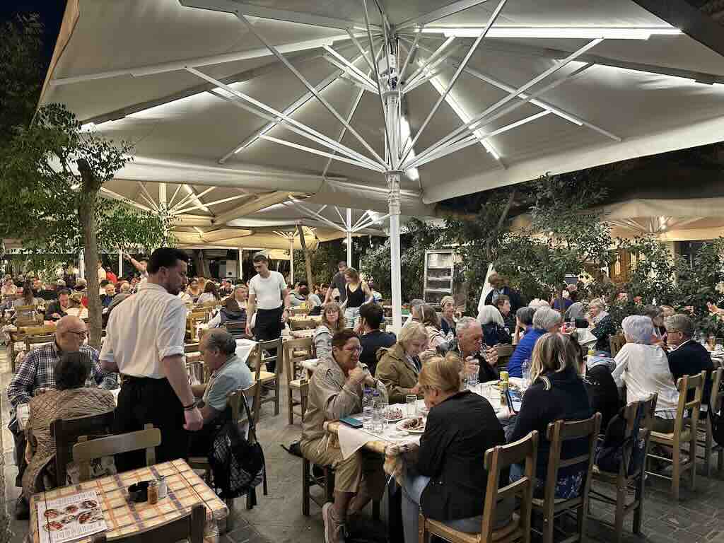 Busy traditional Greek taverna in Athens at night with people dining outdoors under umbrellas