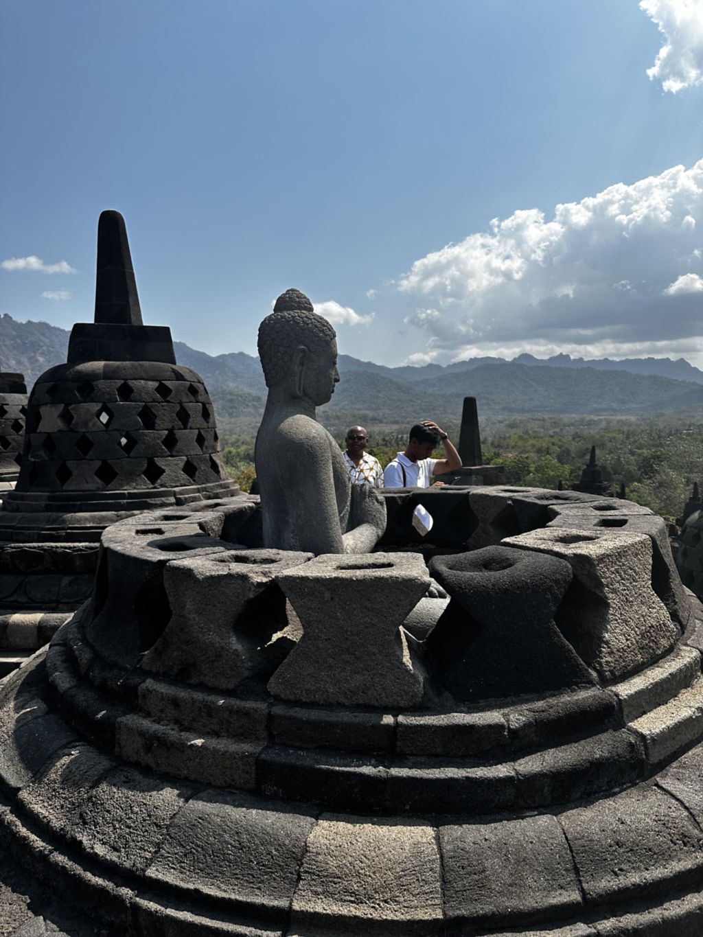 A seated Buddha statue visible inside an opened bell-shaped stupa on the upper terrace of Borobudur, Java, Indonesia