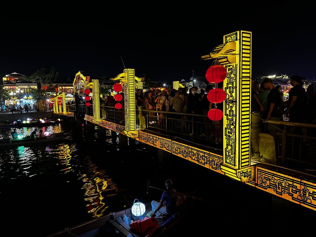 De An Hoi-brug in Hoi An 's nachts geel verlicht, met een lampionnenboot eronder