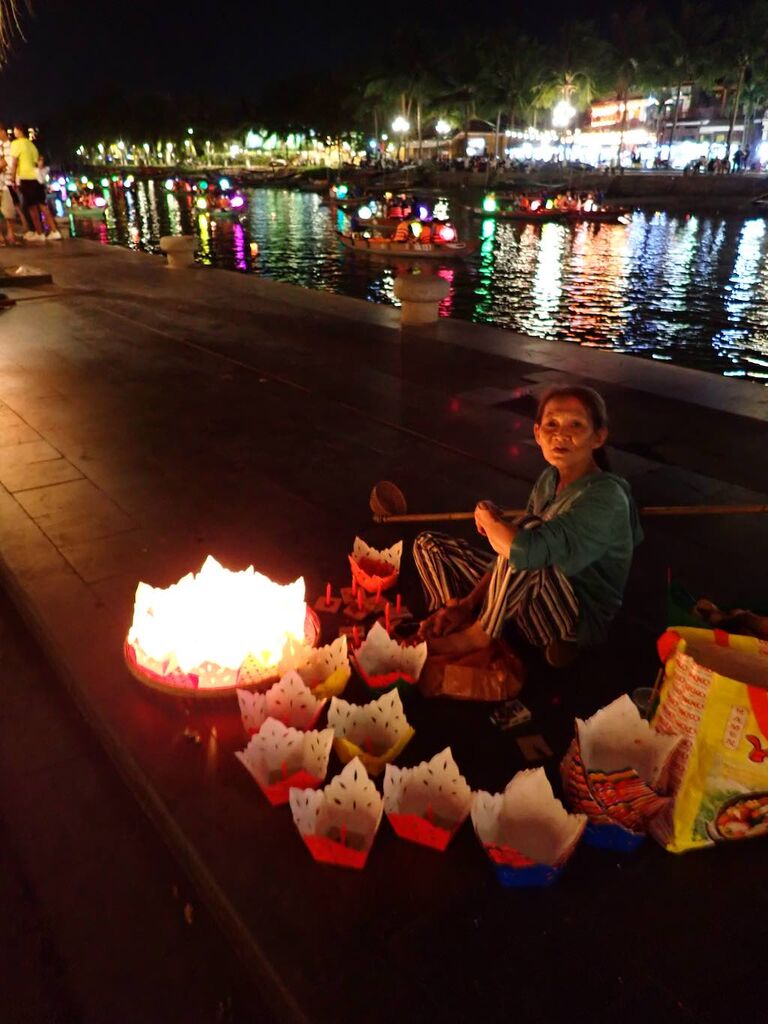 Een vrouw verkoopt 's avonds gevouwen papieren lotuslampionnen aan de oever van de Hoai in Hoi An