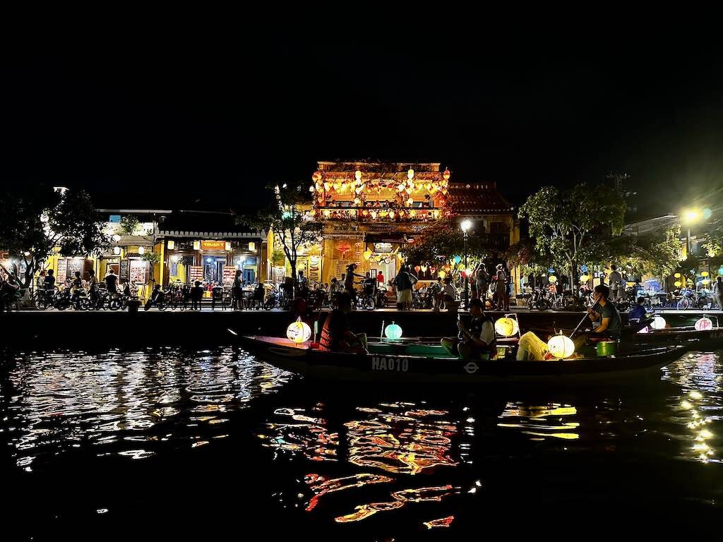 Roeiboot vol papieren lampionnen op de Thu Bon bij nacht, voor een verlicht Chinees verenigingshuis in Hoi An