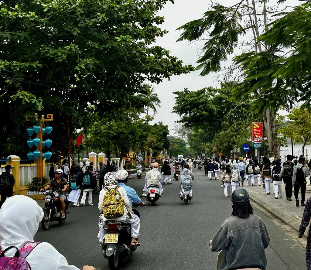 Vietnamese scholieren in witte ao dai lopend en op scooters op weg naar huis in Hoi An