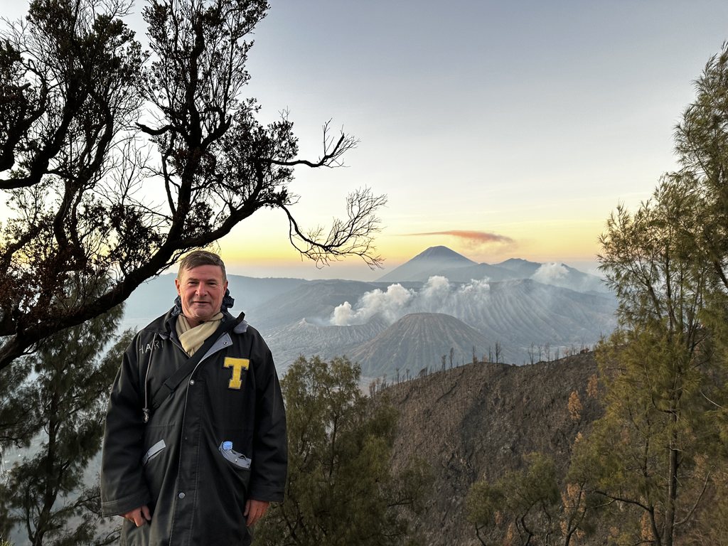 Mount Bromo die gas uitstoot naast Mount Batok met daarachter een uitbarstende Semeru, gezien bij zonsopgang vanaf de calderarand