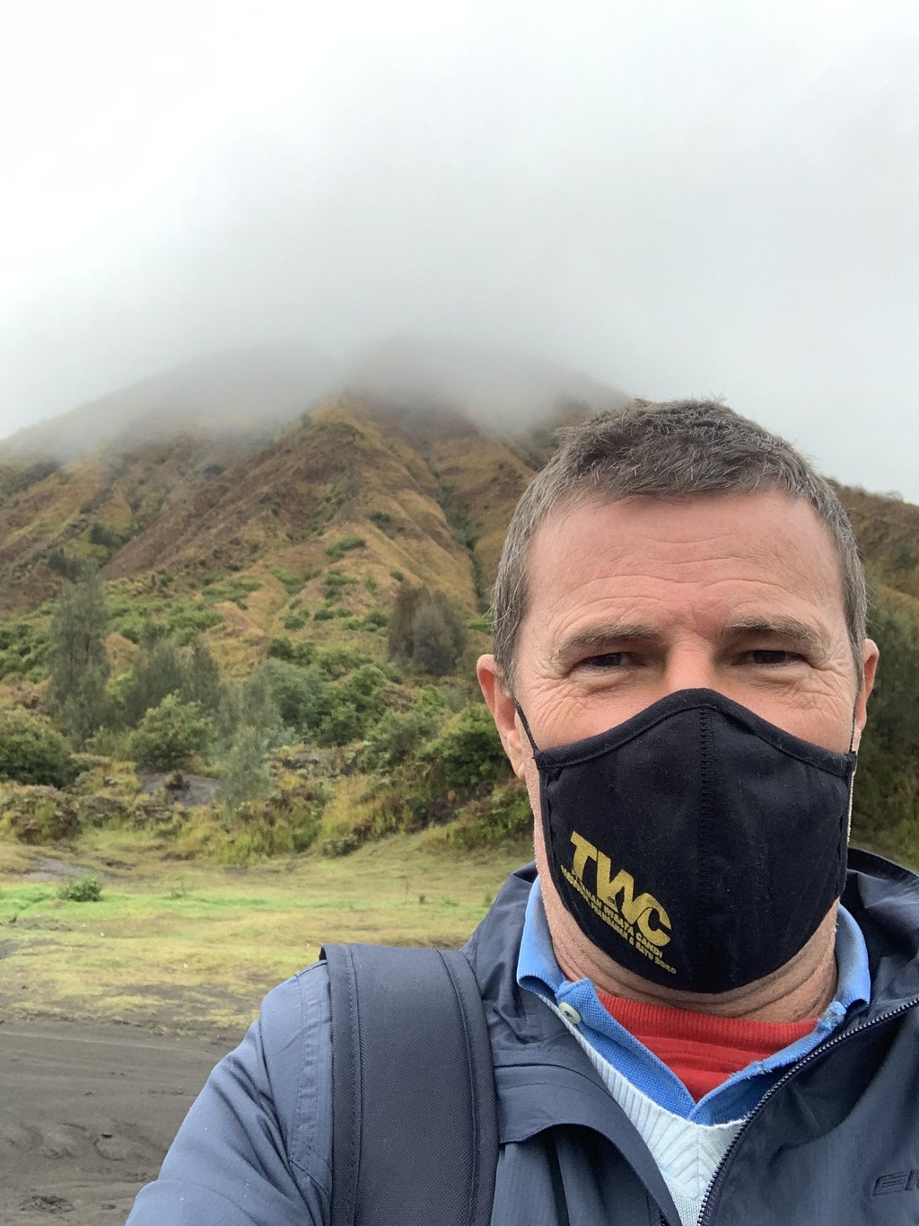 Blaise Jaeger met mondkapje op Mount Bromo in januari 2021, met achter hem een groene bergkam die verdwijnt in de wolken