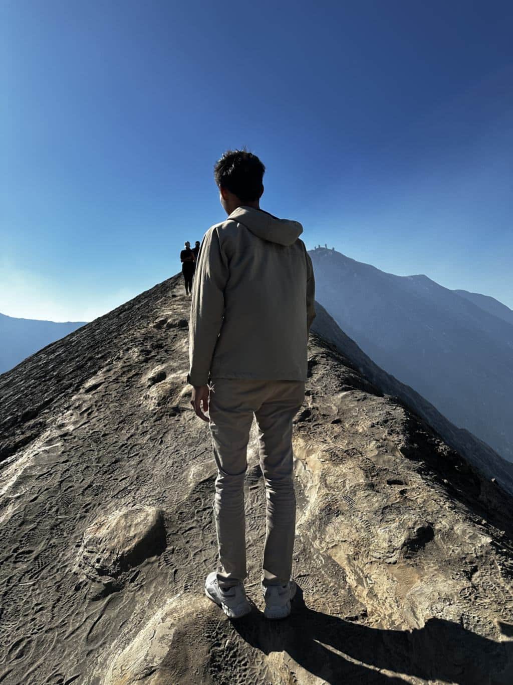 Een bezoeker op de smalle rand van de krater van Mount Bromo met de calderawand daarachter, Oost-Java