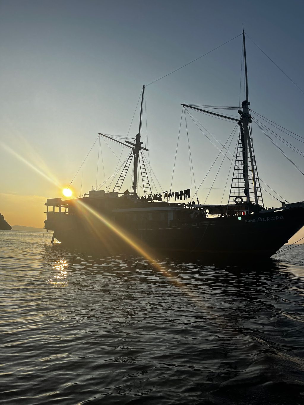 Silhouette di una goletta phinisi contro il tramonto al largo del Sulawesi del Nord