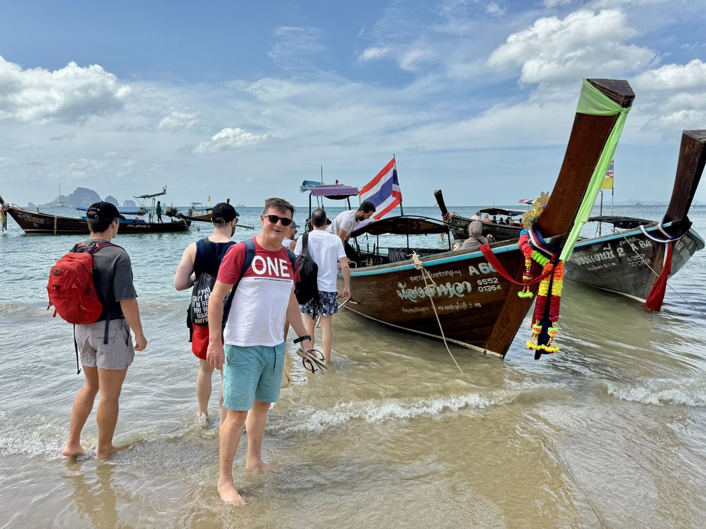 Passageiros entrando na água para subir em um longtail na praia de Ao Nang rumo a Railay