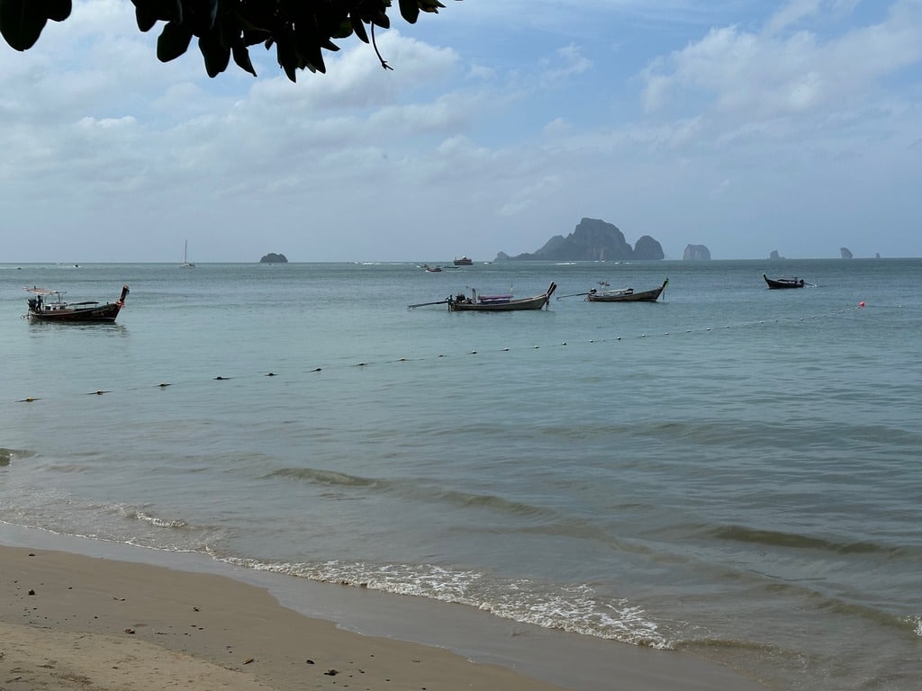 Mar calmo pela manhã e barcos longtail na praia de Ao Nang, Krabi