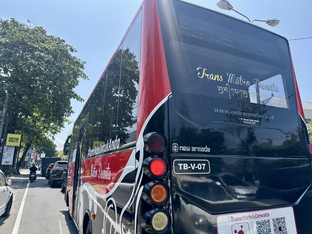 Achterkant van een rood-zwarte Trans Metro Dewata-bus in een straat in Denpasar, met de naam van het netwerk en een QR-code