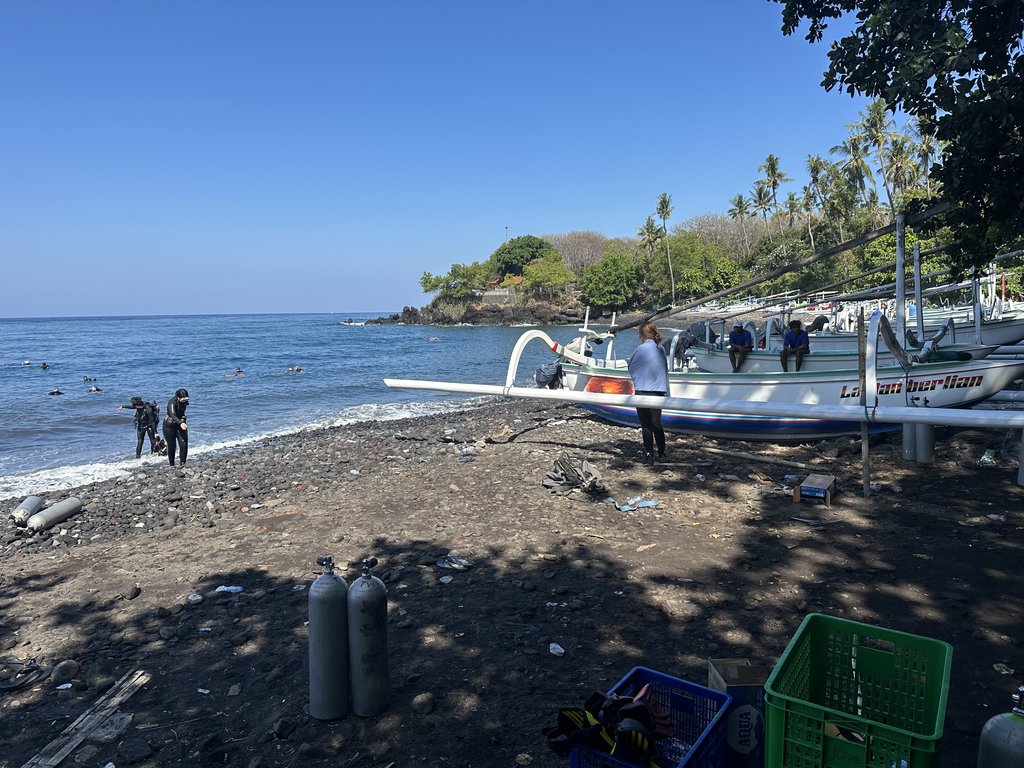 Spiaggia di ciottoli neri a Tulamben con una piroga jukung e sub che entrano in acqua