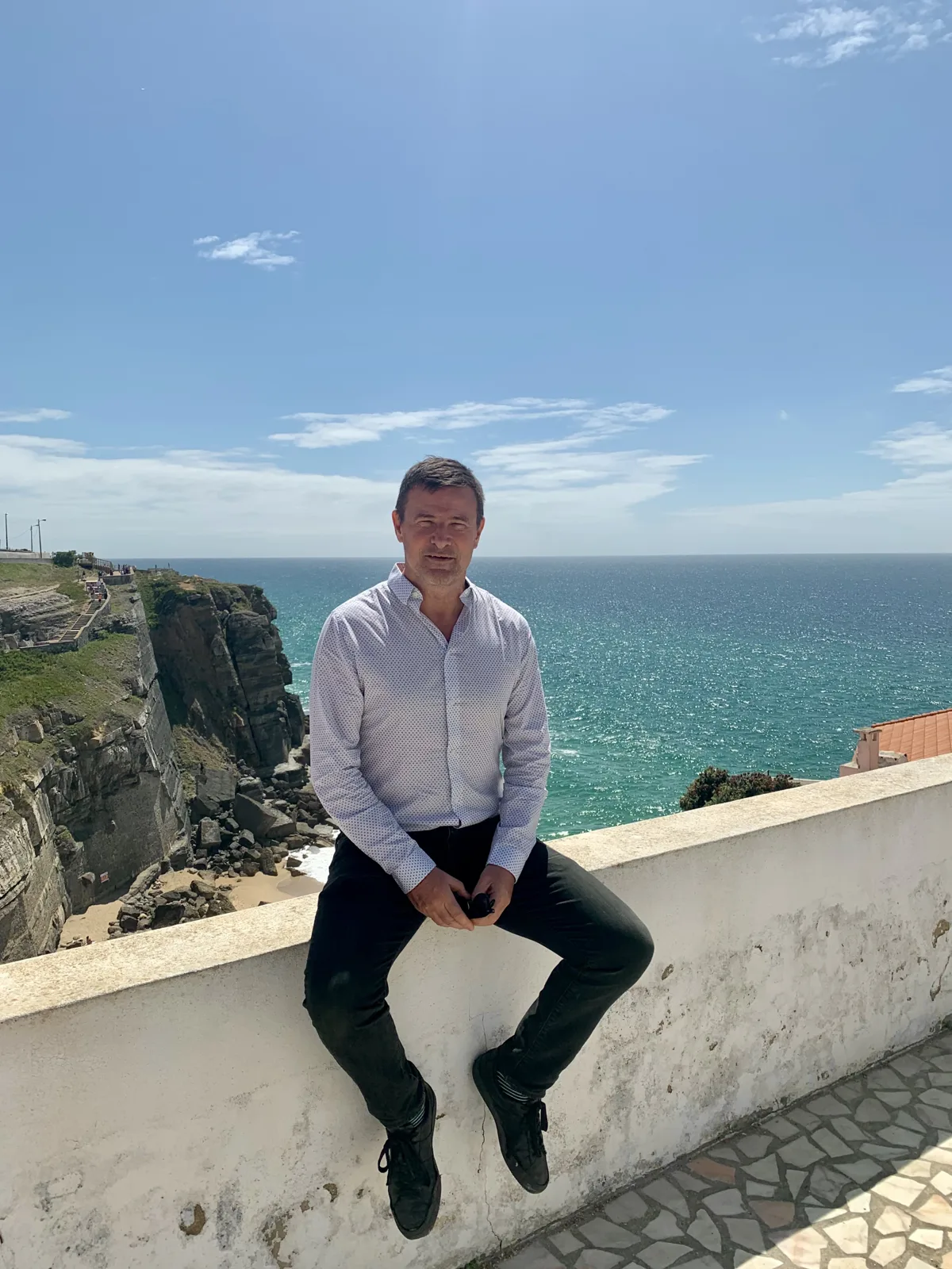 Blaise Jaeger sitting on a wall above the cliffs and the ocean at Azenhas do Mar