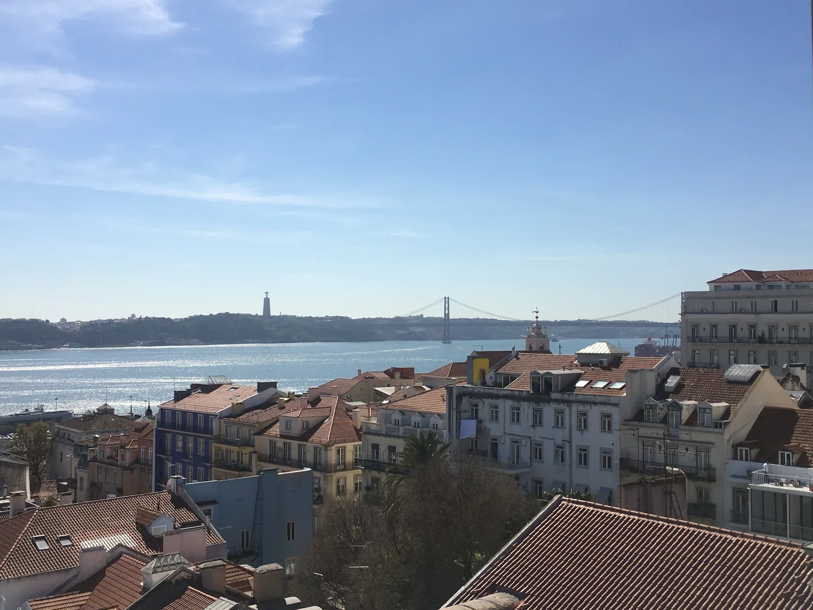 The roofs of Chiado and the Tagus with Cristo Rei seen from a rooftop terrace