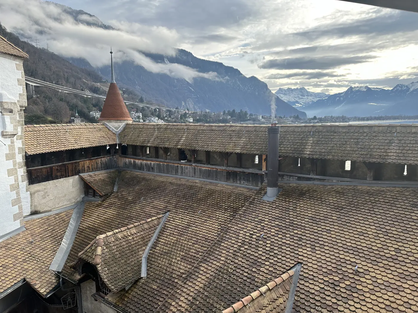 The roofs and towers of Chillon Castle with Lake Geneva and the Alps in the clouds