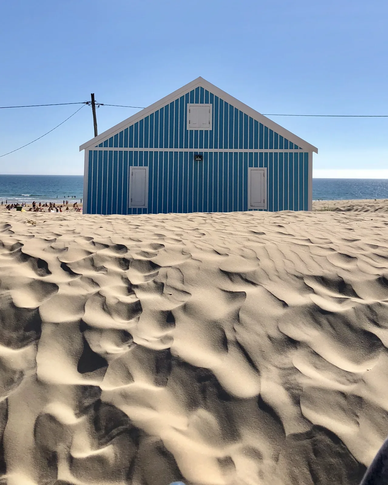 A blue wooden beach hut on the rippled sand of the Costa da Caparica