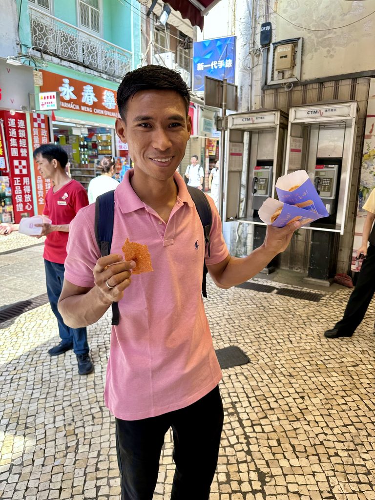 Roy在澳门街头拿着免费试吃的猪肉干和一袋蛋挞