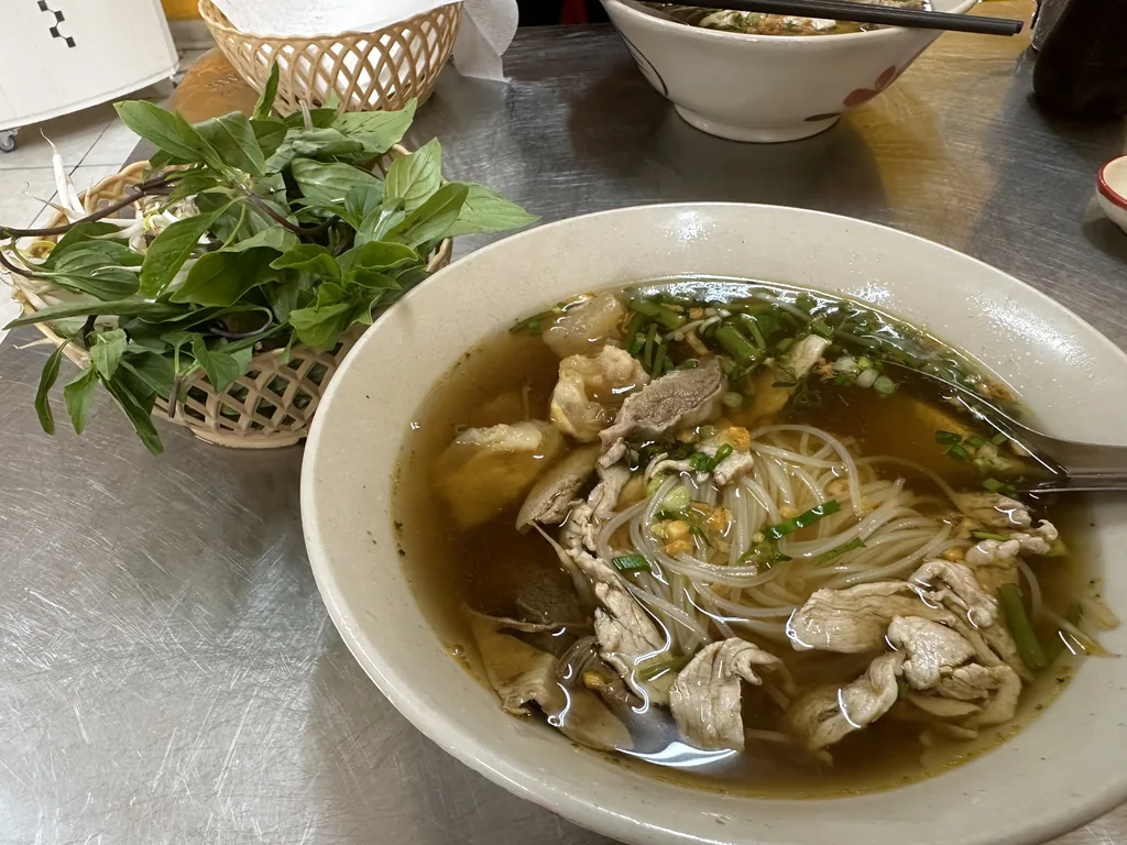 Hu tieu-noedelsoep met varkensvlees en een mandje verse kruiden in Cholon, Saigon