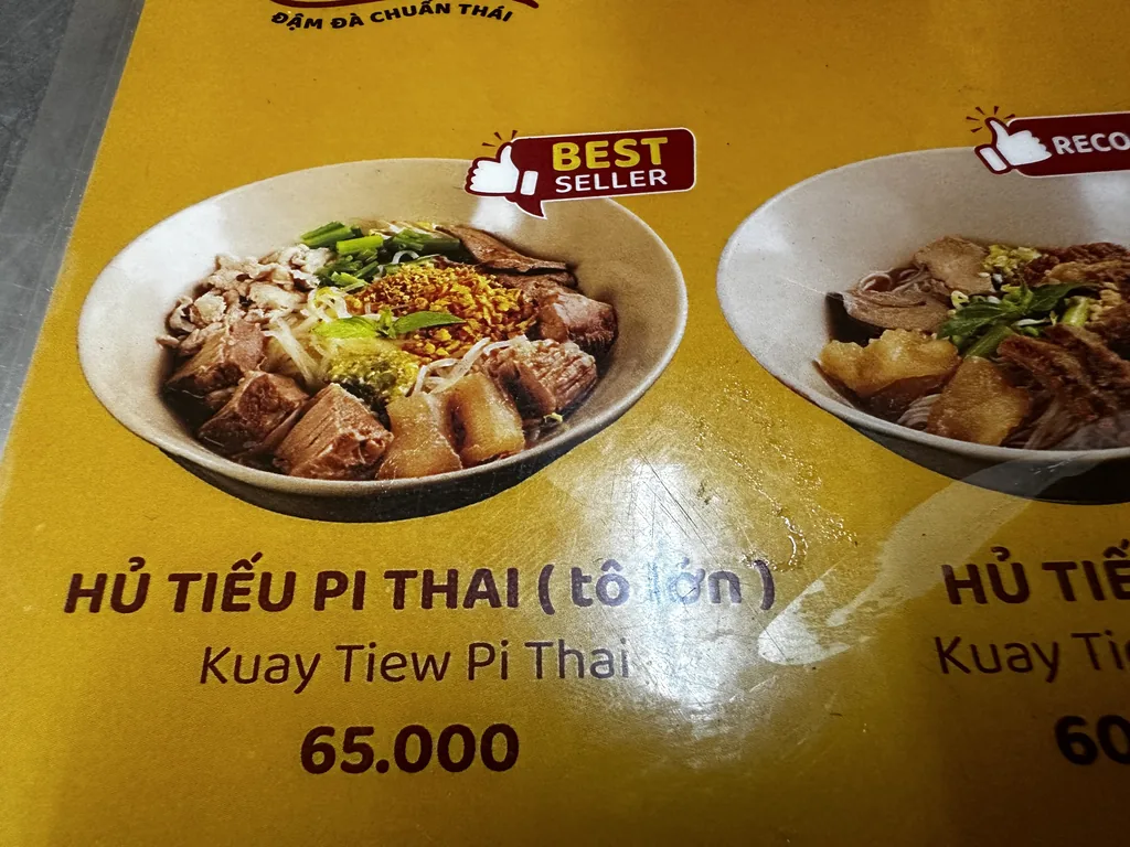 Menukaart van Pi Thai met een grote kom hu tieu voor 65.000 VND in Saigon