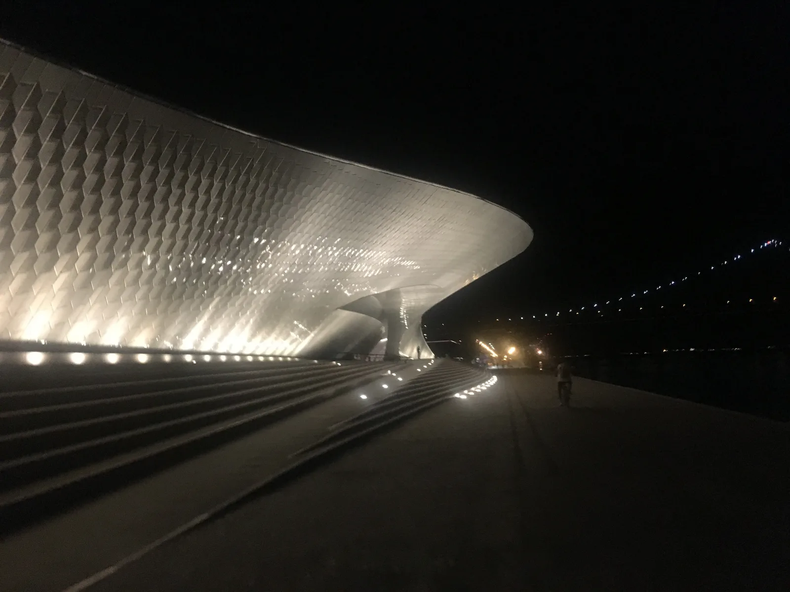 The illuminated curved roof of the MAAT museum at night on the Tagus in Belém