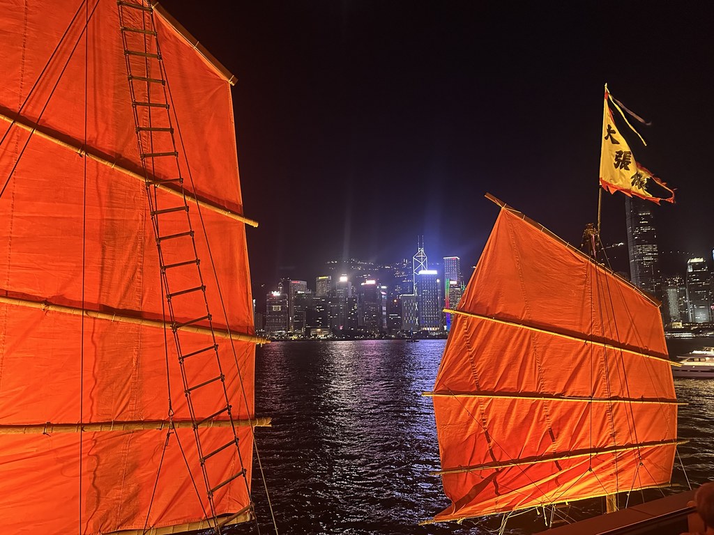 夜晚维多利亚港上的红帆船,身后是灯火通明的港岛