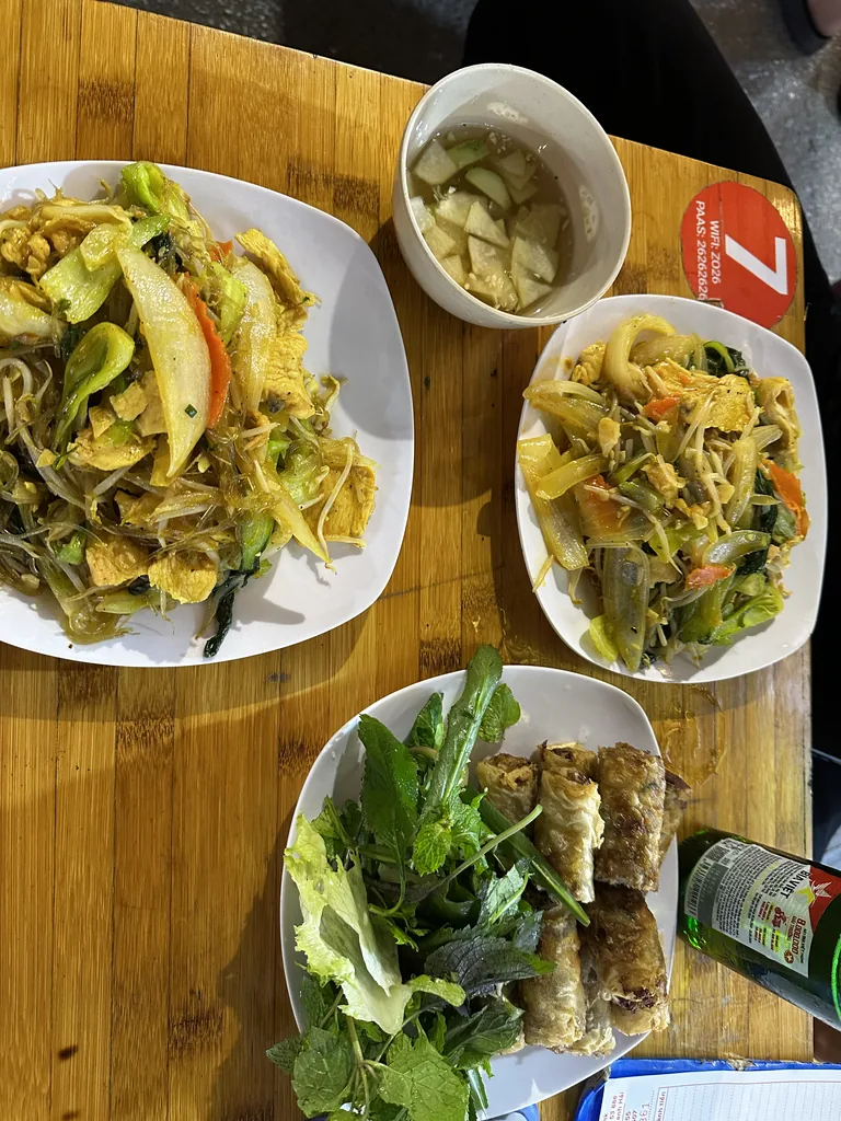 Twee borden gebakken noedels en gefrituurde loempia’s met kruiden en een Hanoi-biertje