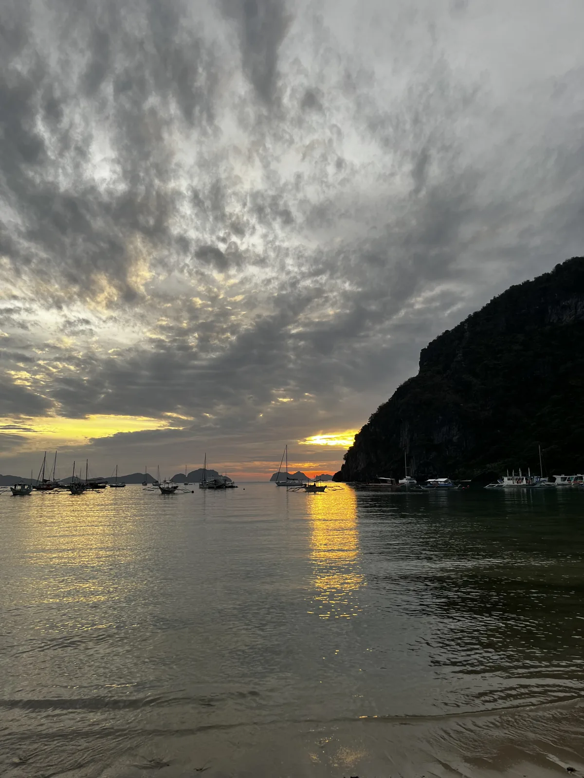 Tramonto sulla baia di El Nido con barche all’ancora e una falesia calcarea