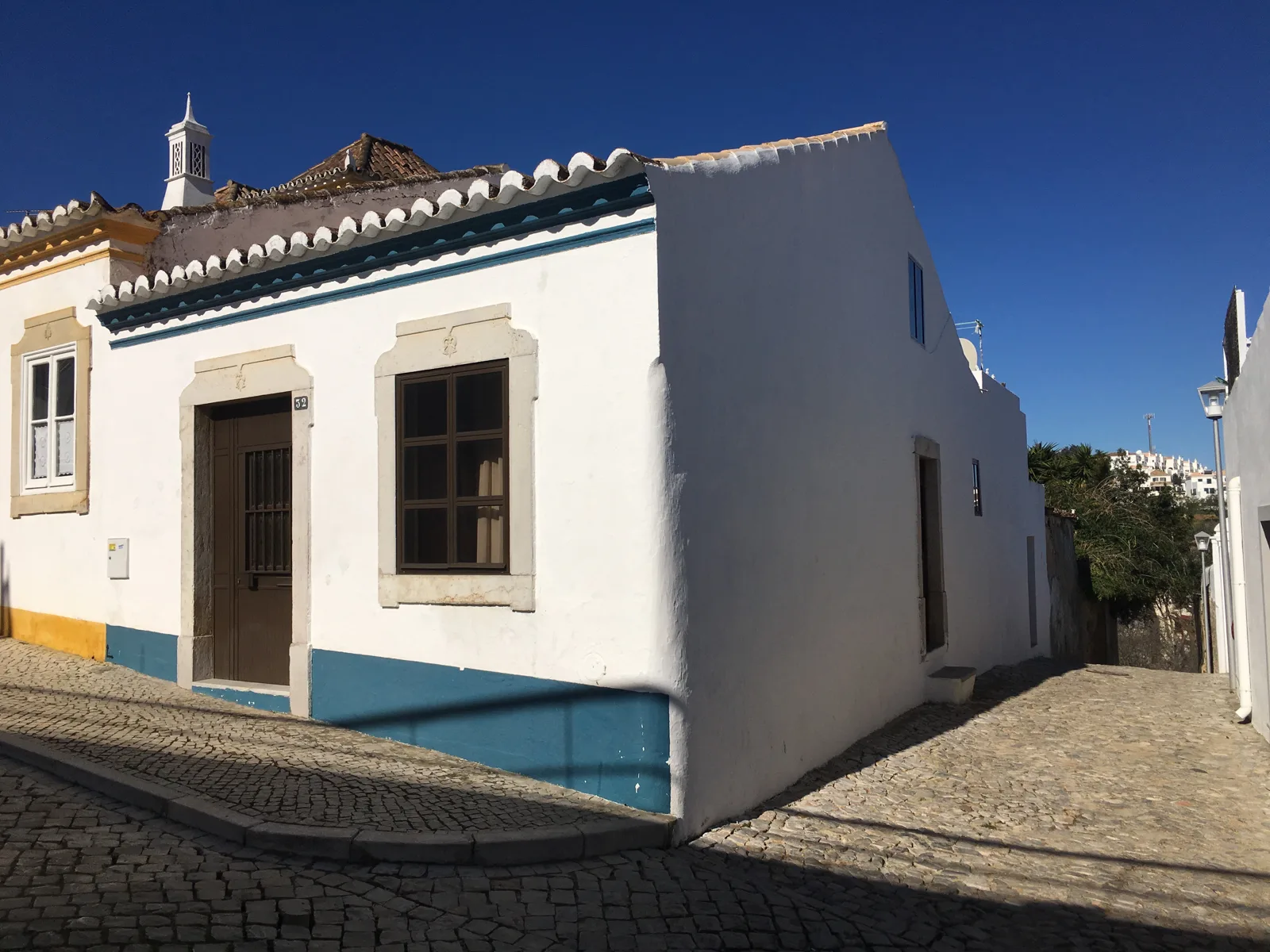 A white house with blue trim on a cobbled street in Tavira