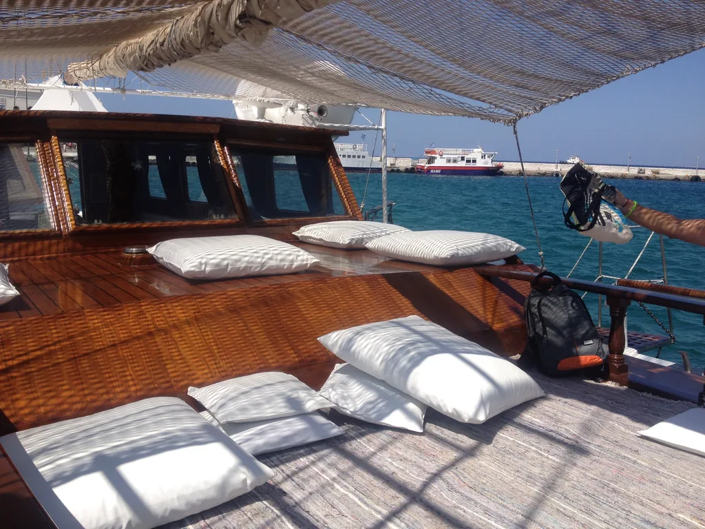 Deck of a wooden caique with white cushions moored in Mykonos harbor